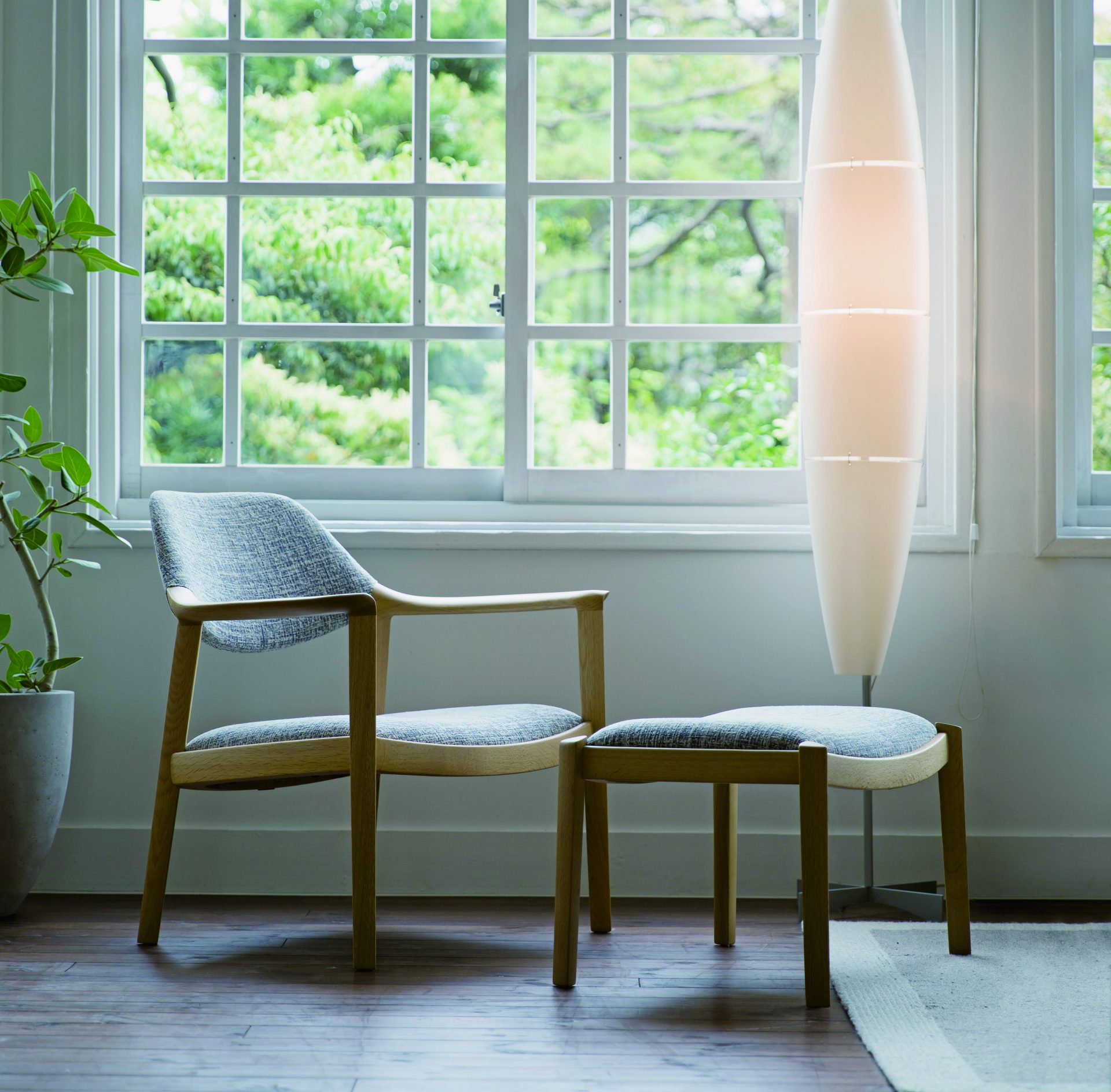 A lounge chair with a stool by the window. They are placed close to the window. The abundant light sheds upon them.