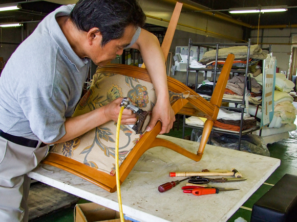 Our craftsperson is re-upholstering a dining chair with a special tool. It's a chair returned from a customer for restoration.