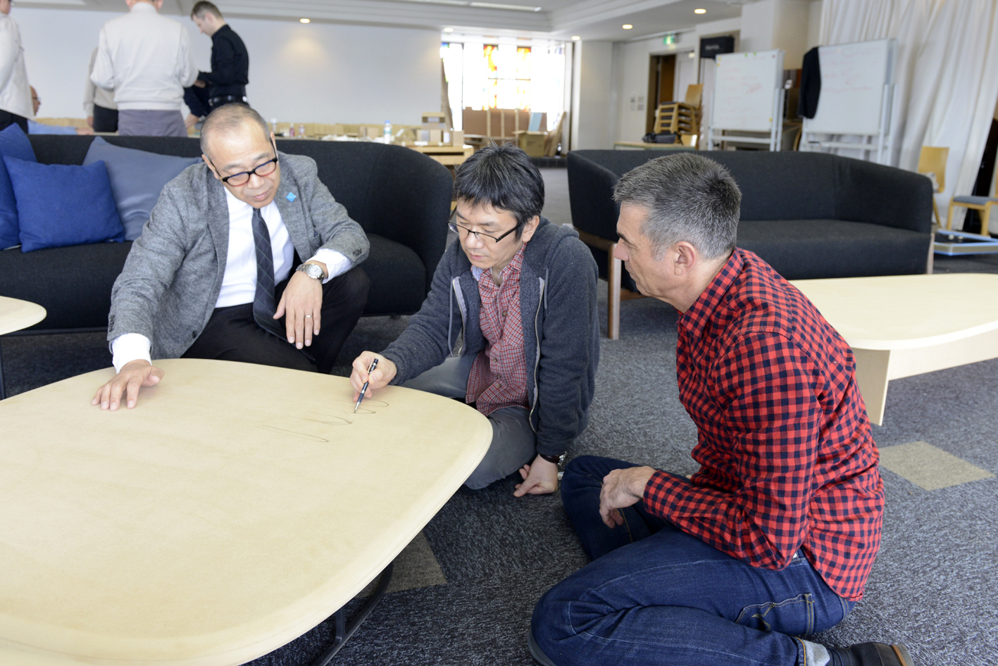 Three guys are talking about something around a coffee table. The man in a red shirt is the designer of the coffee table.