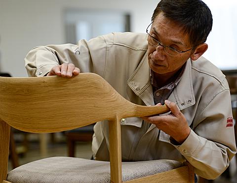 A craftsman is conducting a final inspection on a wooden chair.