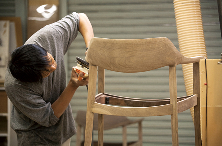 Our craftsperson is applying a sanding tool on the wooden frame of a dining chair.