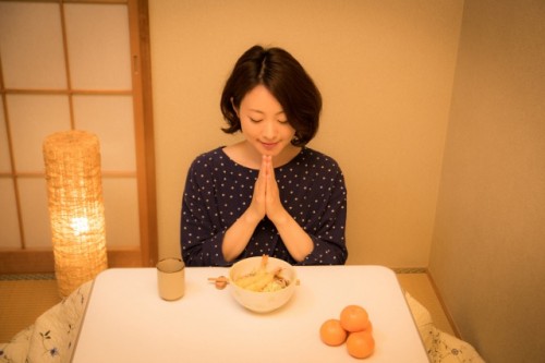 A woman just starting to eat a noodle dish with her hands clasped.