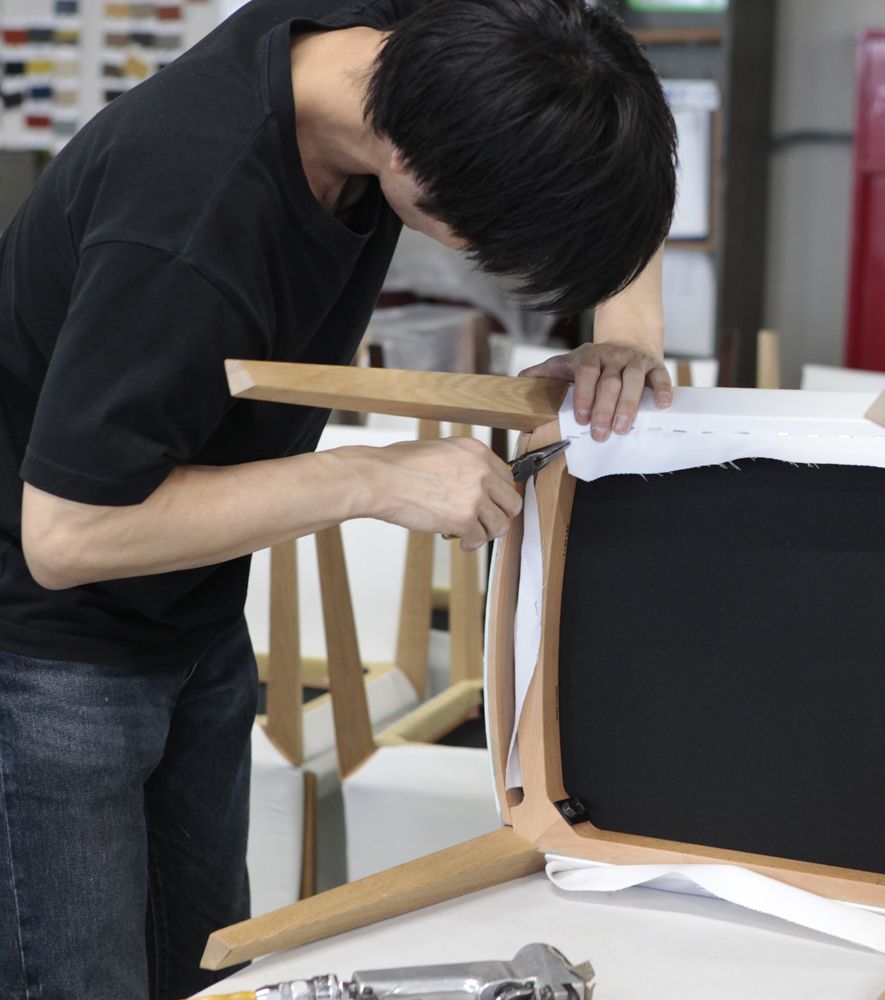 Our factory staff is upholstering the seat of a dining chair with a staple gun.