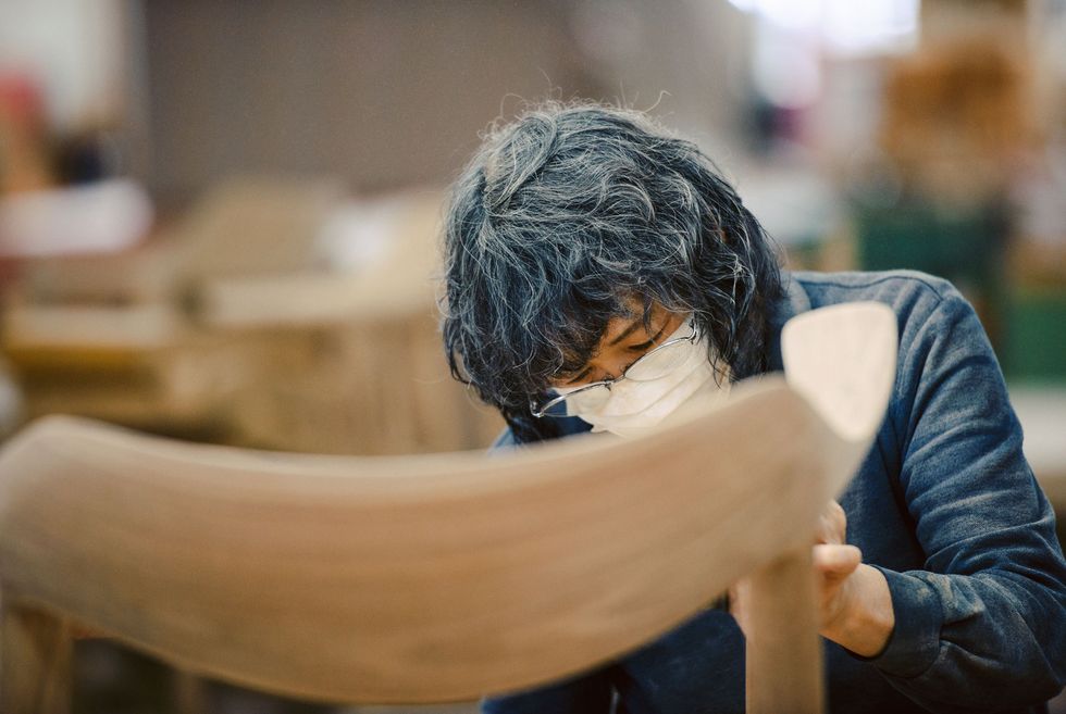 A woman is sanding the surface of a wooden chair.