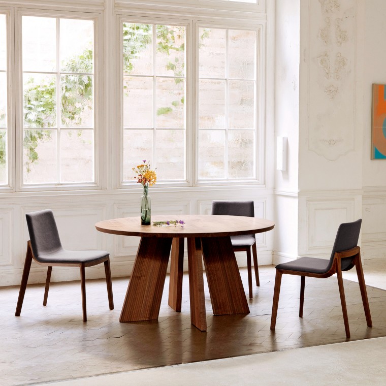 A round table with three dining chairs by the window. There is a flower vase on the table.