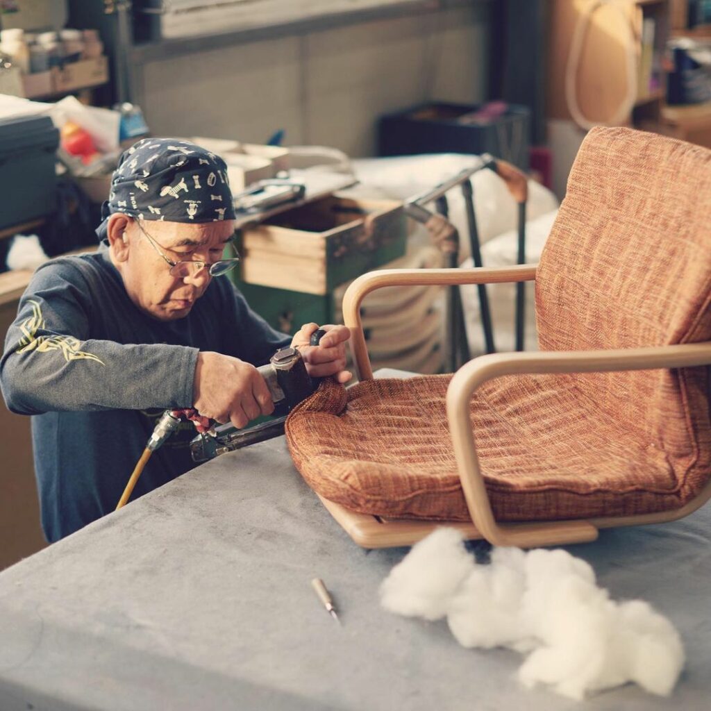 A craftsman is upholstering a chair.