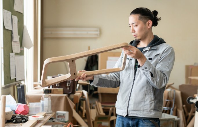 A craftman is checking the wood part of a chair frame.