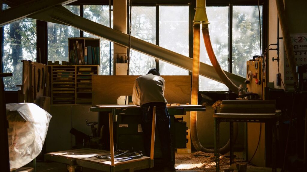 Our craftsperson is working on something on the working table. It's by the window, and the light of a sunset is shedding on his back.