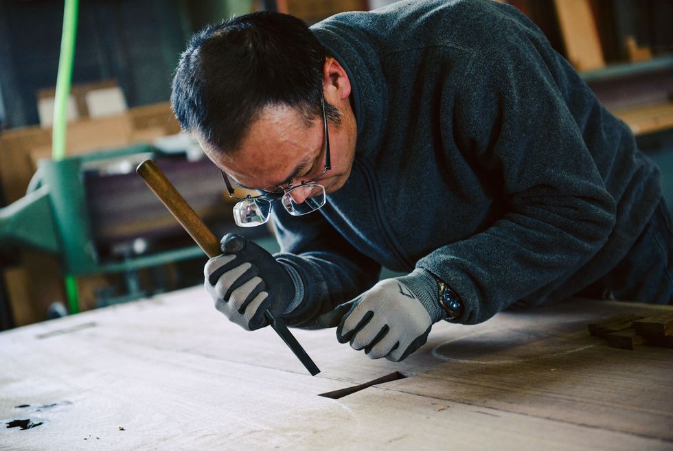 Our craftsperson is gouging a hole on the backside of a dining table.