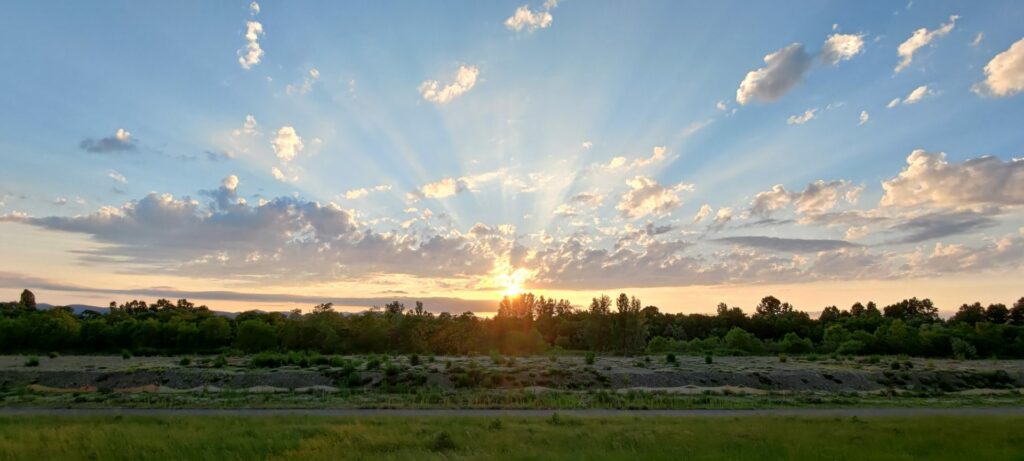 The sunrise over the field and forest. The light is penetrating some clouds.