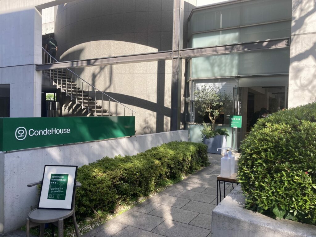 The image of a shop entrance. On the concrete wall, there's a green signboard saying CondeHouse.