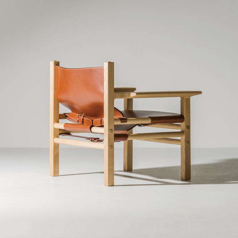 A wooden chair with light-color wood and reddish brown leather. The thick leather works as a part of the structure.