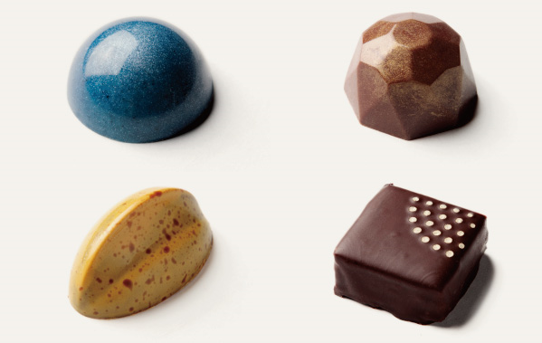 Four pieces of beautiful chocolate: : local-made blue cheese in the blue one; local sake in the polygon-shape one; caramel made from local pear in the yellow one; local-made honey in the square one.