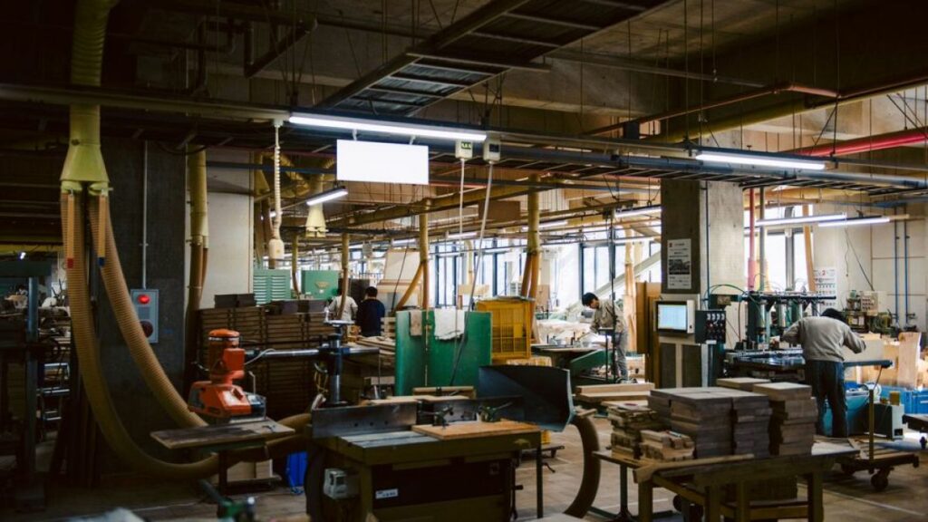 A furniture factory where some people are working. The place looks to be packed with many machine tools.