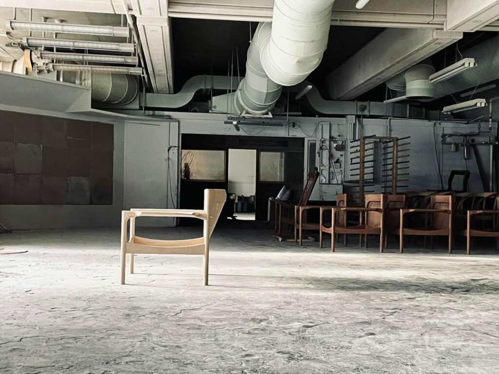 A wooden chair frame is placed solely in the middle of a painting booth.