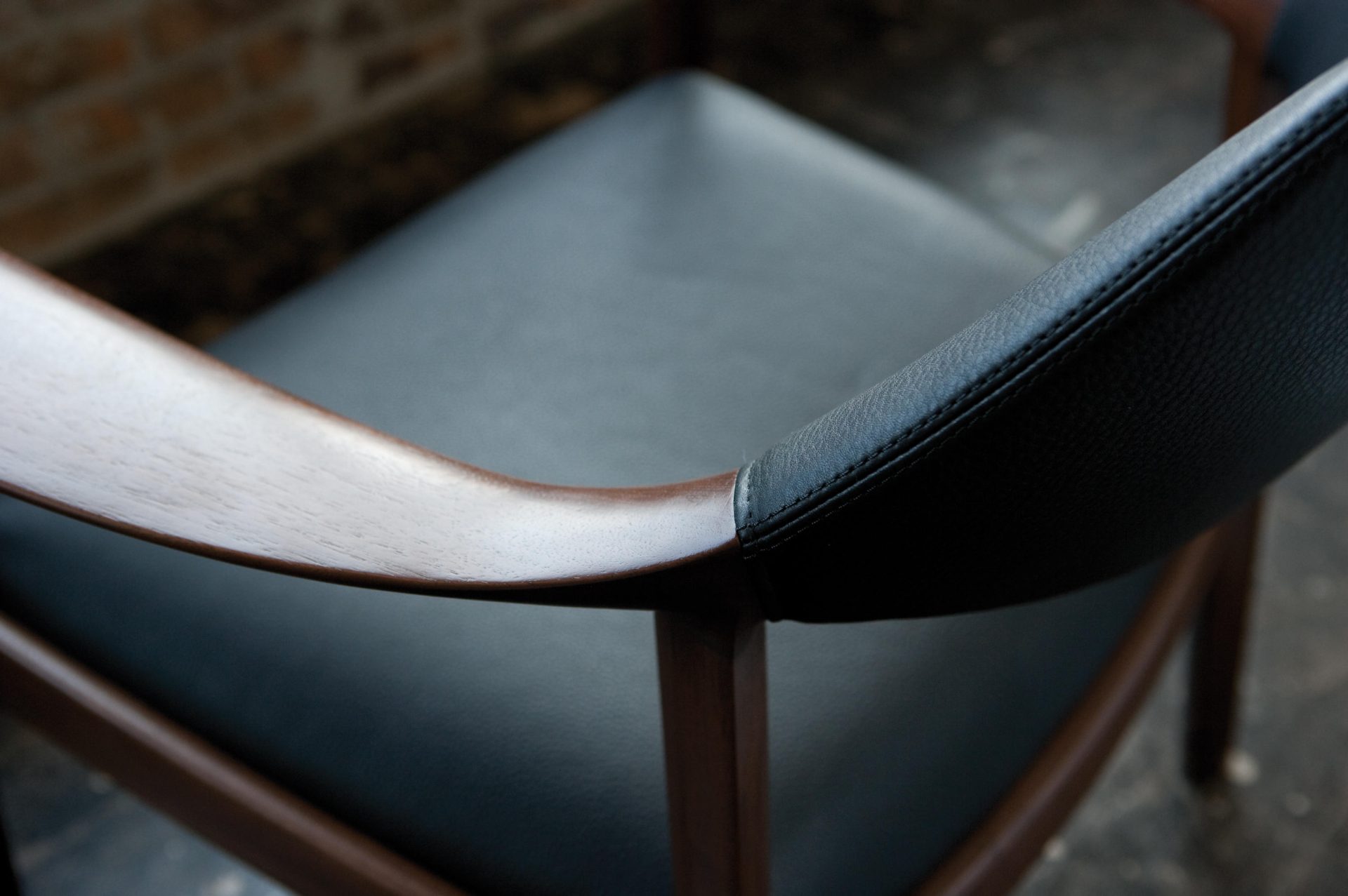 A dining chair upholstered with black leather. The beautiful line from the backrest to the left arm is focused. 