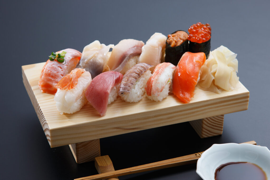 There are 12 pieces of various kinds of sushi on a wooden plate