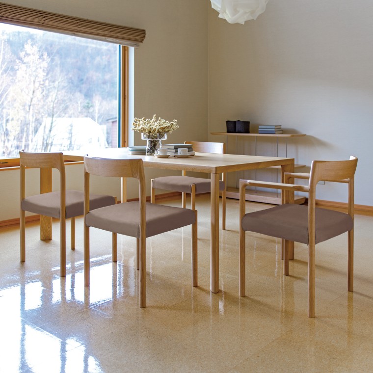 A white oak dining table with four dining chairs by the window. On the table are some books, cups, and a flower vase.