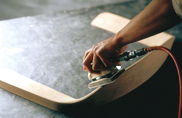 An electric sander is applied to a wooden backrest under process.