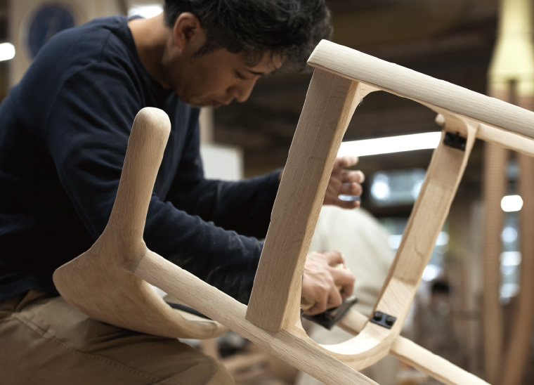 Our craftsman is sanding on a wooden chair frame. The chair is our best-selling one, WING.