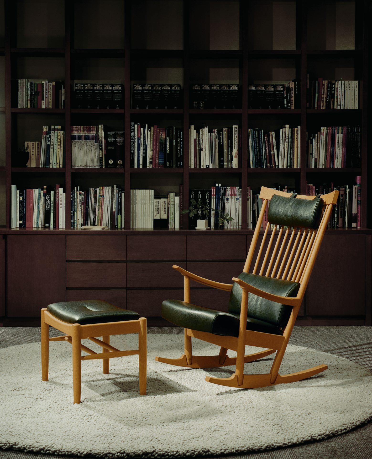 A rocking chair with a stool is placed in front of a big book shelf. There are many books on the shelf.