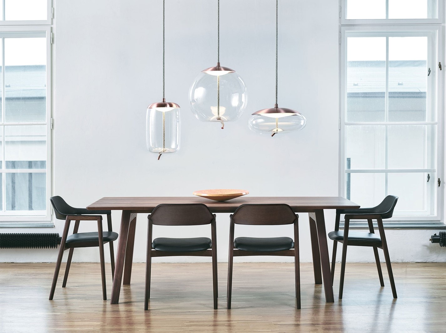 A dining table with four dining chairs, over which there are three pendant lamps are hung