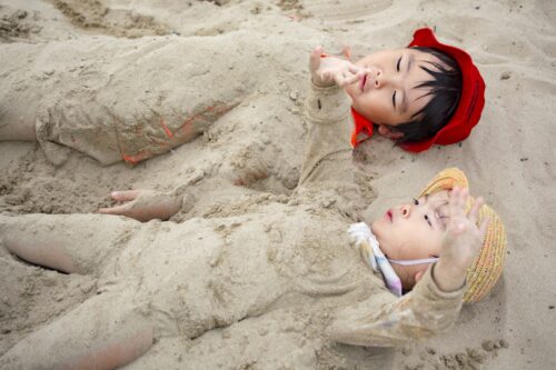 Two kids are covered in sand