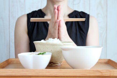 Behind the plate of meal, a woman is clasping her hands.