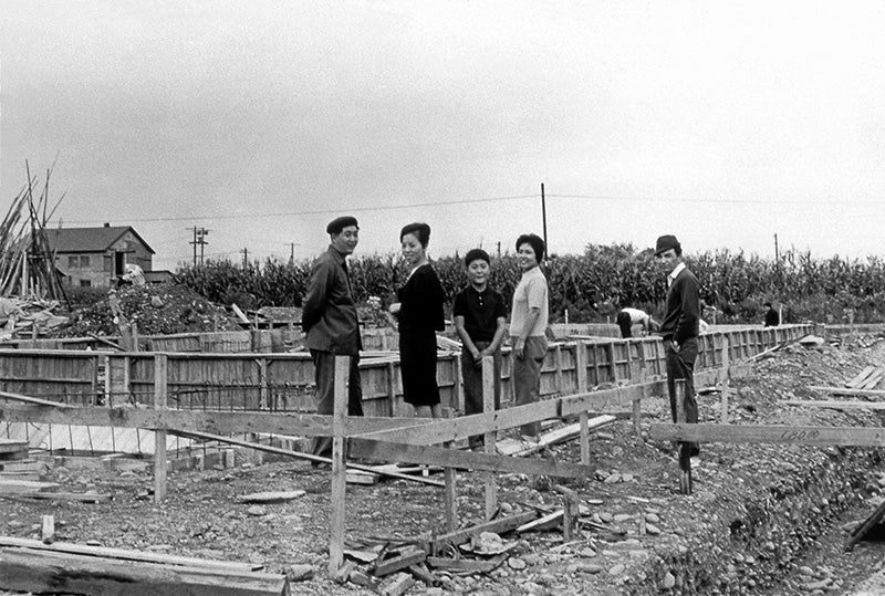 A very old black-and-white picture where five people are in the construction site of their company building