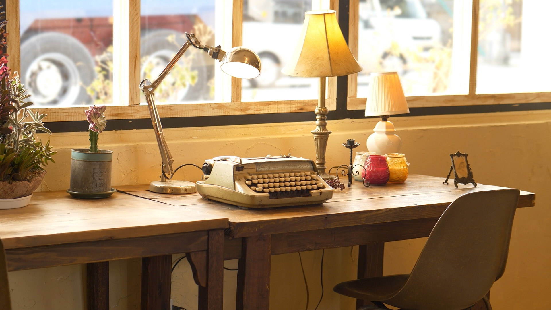 An old typewriter and two lamps are on a desk by the window.