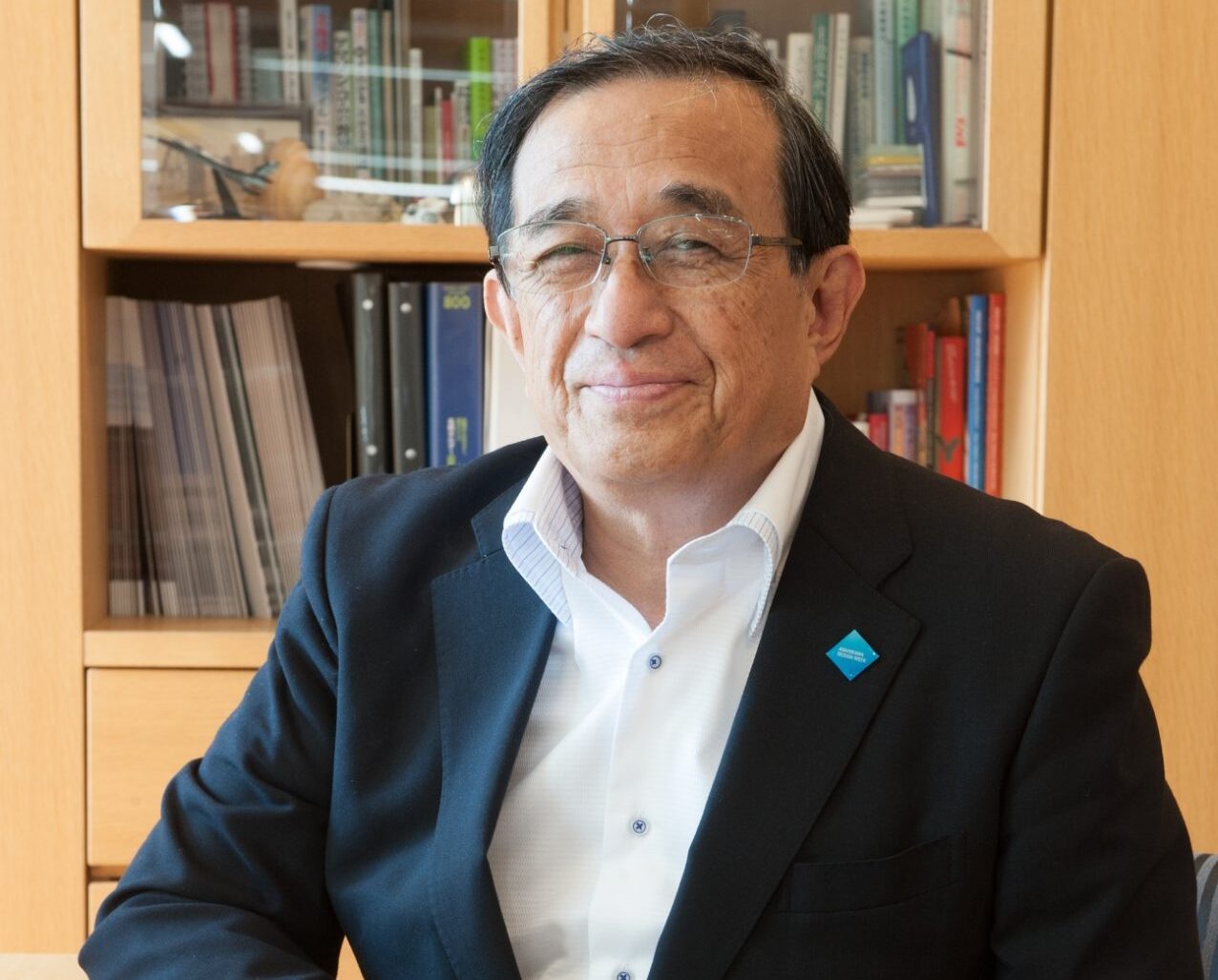 A guy sitting on a chair with his fingers interlaced and facing at the camera