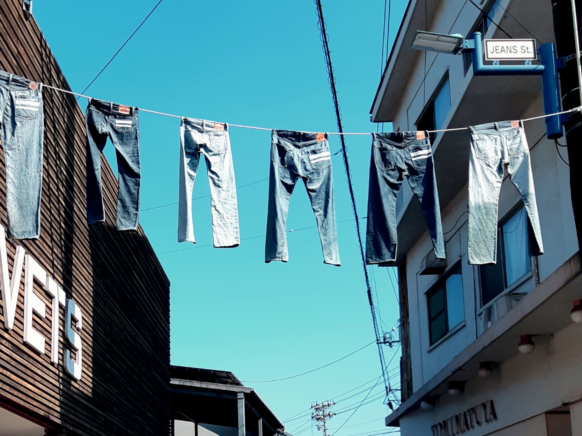 Some pieces of denim jeans are hung on the electrical wire running above the street