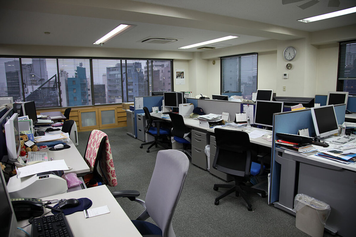 A standard Japanese office room where inorganic gray desks and chairs are orderly aligned.