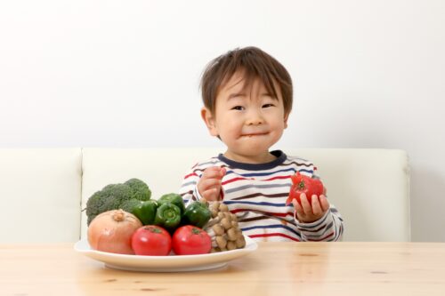 A boy grabbing a red bell pepper in his left hand