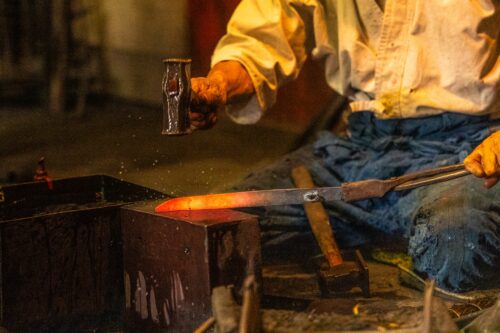 A swordsmith is forging iron heated red.