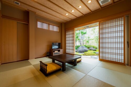 A Japanese traditional room with tatami mats, over which a Japanese traditional courtyard is seen.