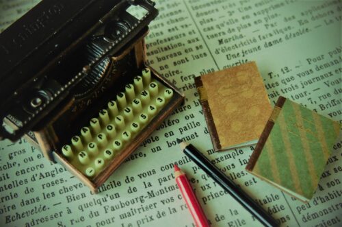 A classic typewriter, notes, and pens are on the newspaper.