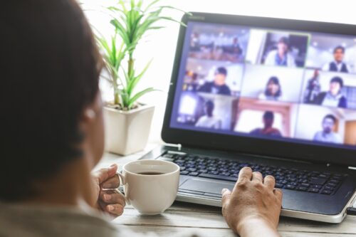 A guy is attending an online meeting, and many people are displayed on his monitor screen.