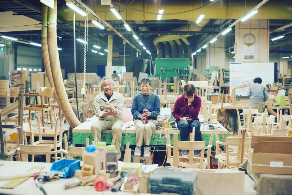 In a furniture factory, three of staff sit on a work table, chatting during a short break.