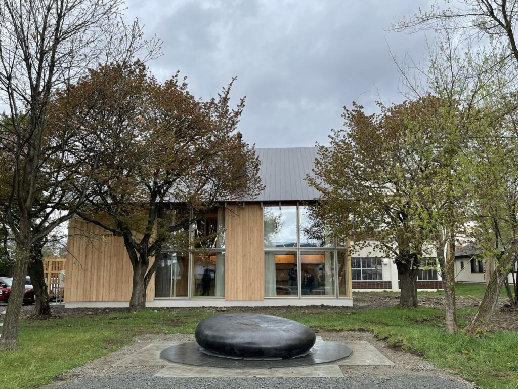 The stylish wooden building desgined by a Japanese famous architect, Kengo Kuma. There is a black stone monument in front of the building.