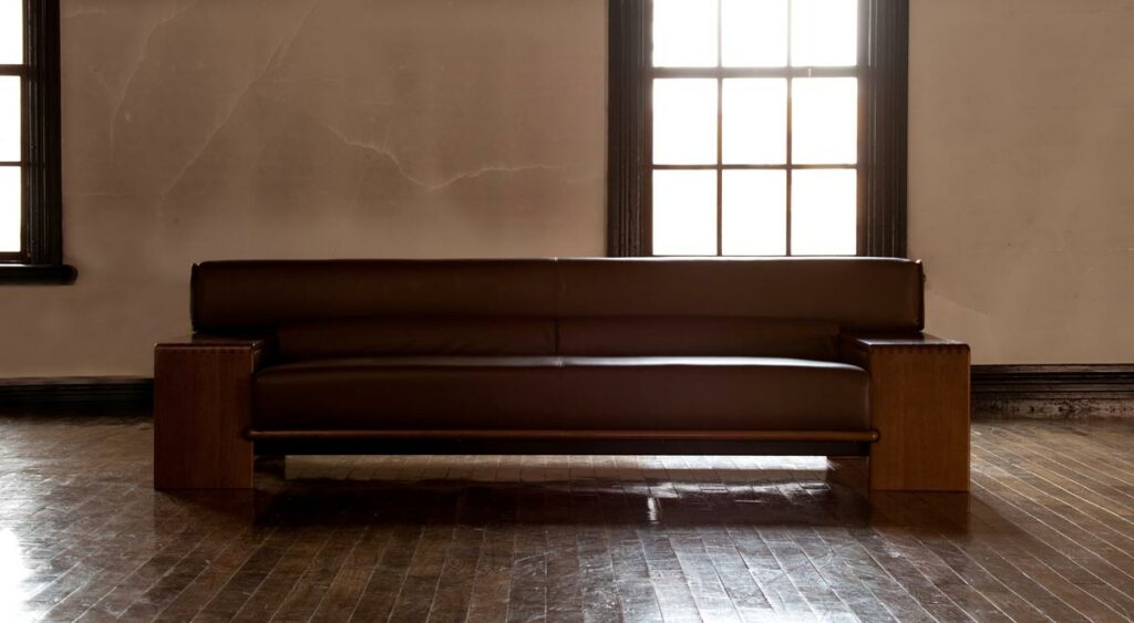 A long sofa is placed on a solid wood floor by the window. It's a backlit photo against the light from the window.