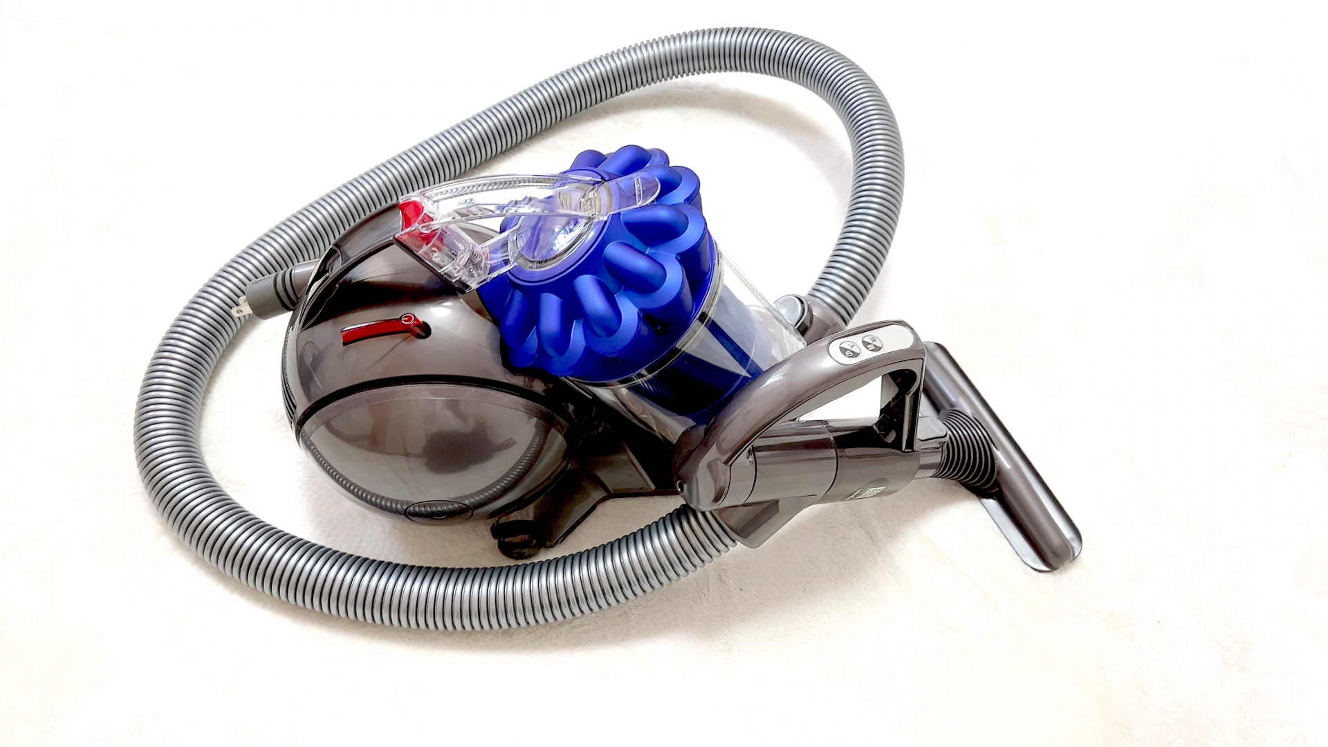A Dyson cordless vacuum cleaner with the transparent dust canister visibly full of swirling dust and hair, suggesting the design provides catharsis by making the cleaning result visible to the user.