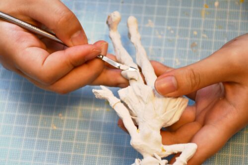Hands are shown, and held and carved in the hands is an anime figurine.