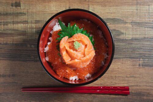 Raw salmon and salmon roe on rice in a bowl with chopsticks