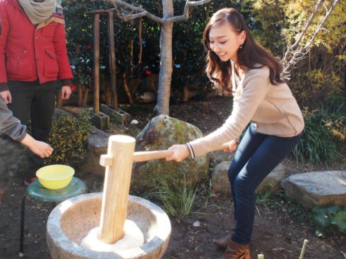A woman is pounding sticky rice to make mochi with a big wooden pestle.