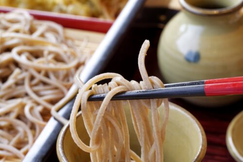 Soba noodle, some of which are held by chopsticks and dipped in the sauce