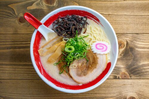A bowl of ramen noodle on top of which there are roasted pork fillet, mushroom, bamboo shoots, and green onion