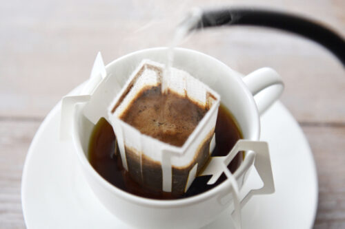 Boiled water is being poured to a coffee drip pack hung on a coffee cup.