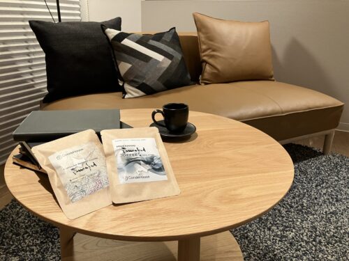 Coffee drip packs are on a coffee table, with a sofa upholstered with light brown leather.